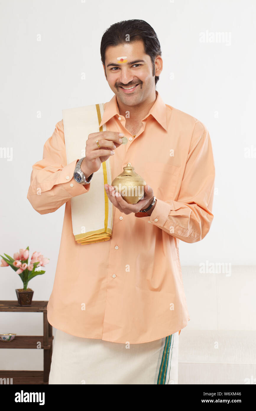 South Indian man inserting a coin into a piggy bank Stock Photo - Alamy