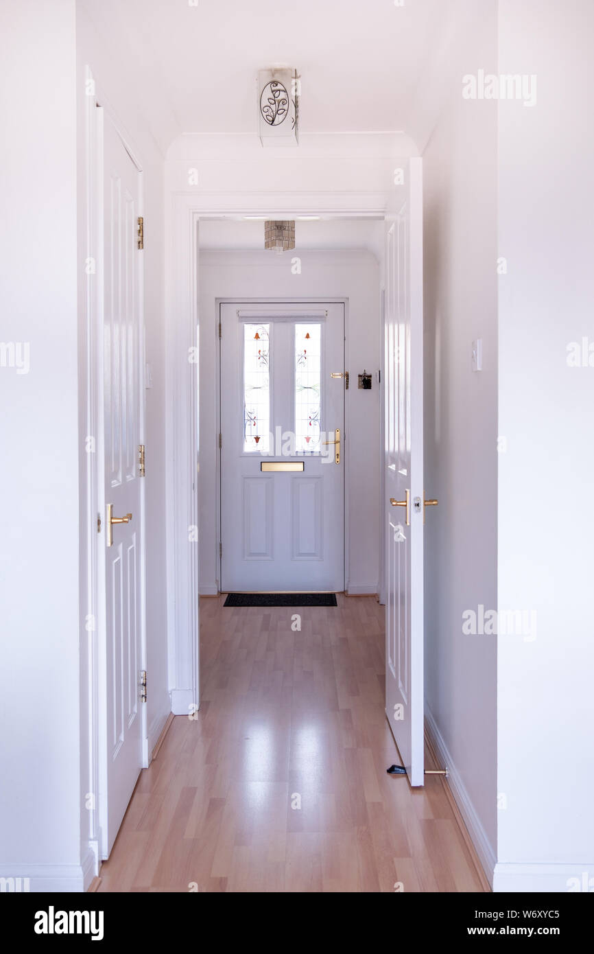 Modern entrance to house with hallway laminated flooring and everything  painted in white clean colours. Door has stained glass inserts to add to  the m Stock Photo - Alamy