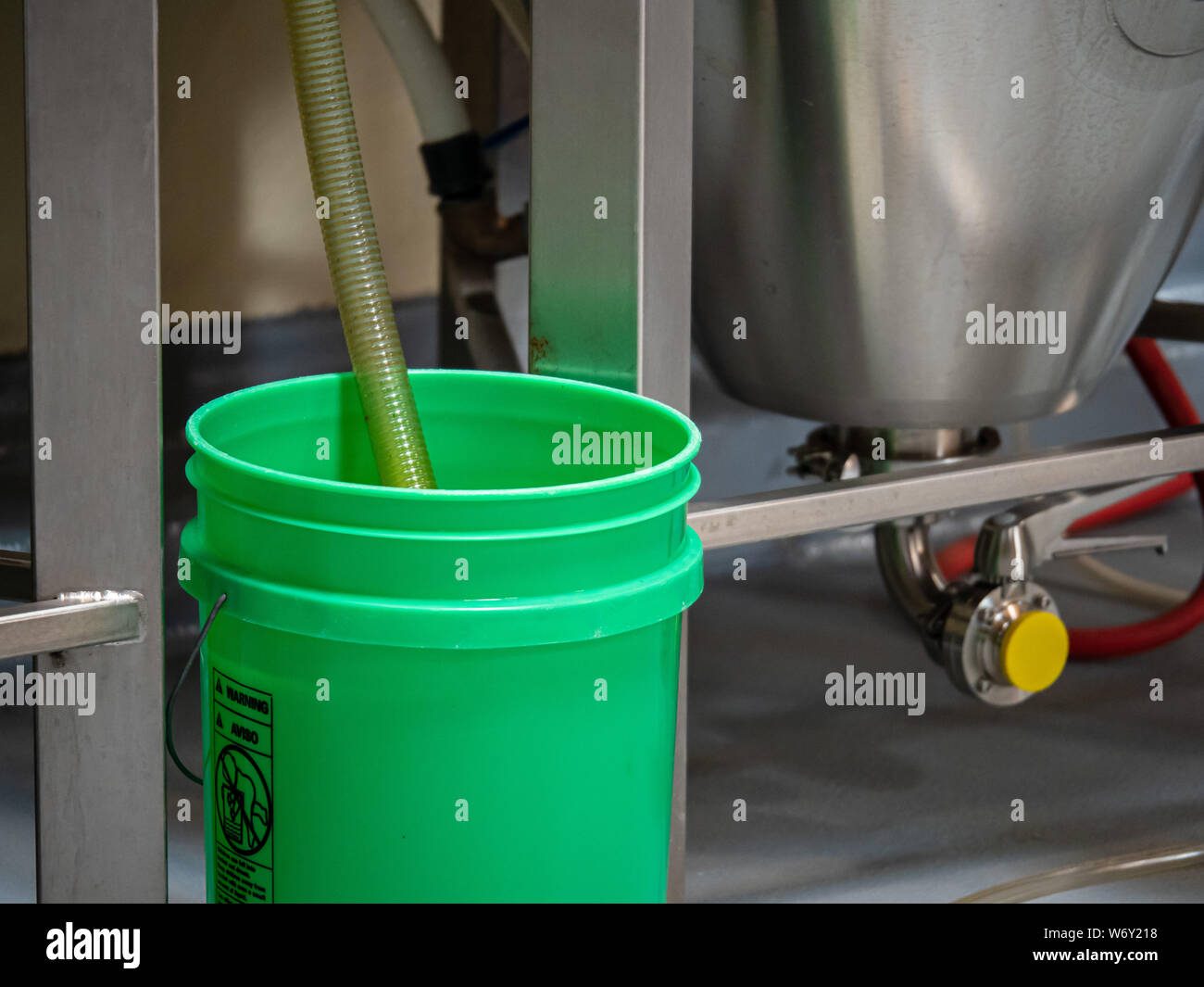 Green bucket with hose running dripping into in industrial setting