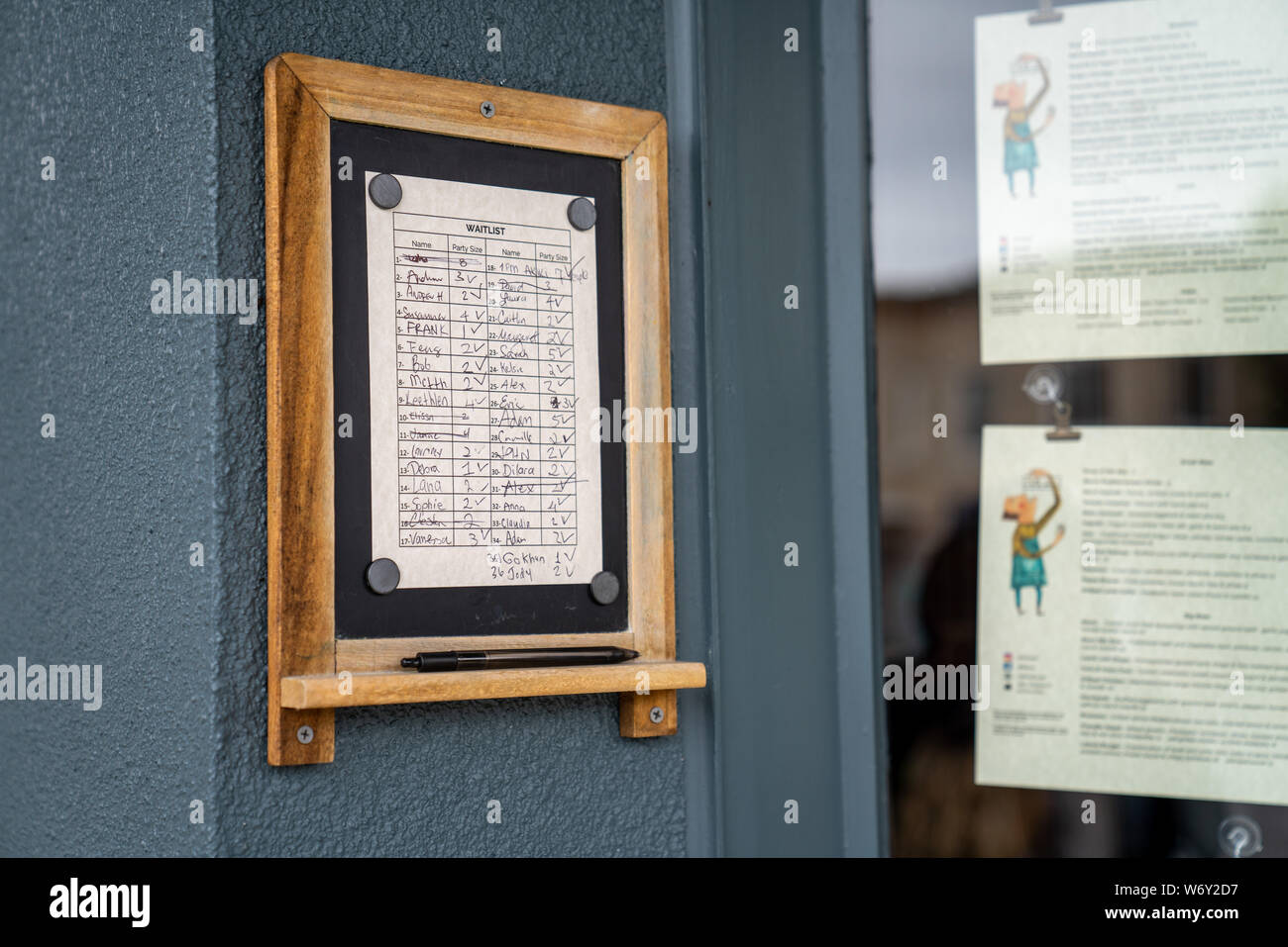 Waitlist filled out with names at popular restaurant next to menus Stock Photo