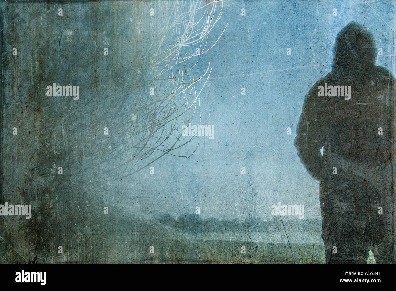 An eerie silhouette of a lone hooded figure in a field With a dark, spooky blurred abstract, grunge, vintage, edit. Stock Photo
