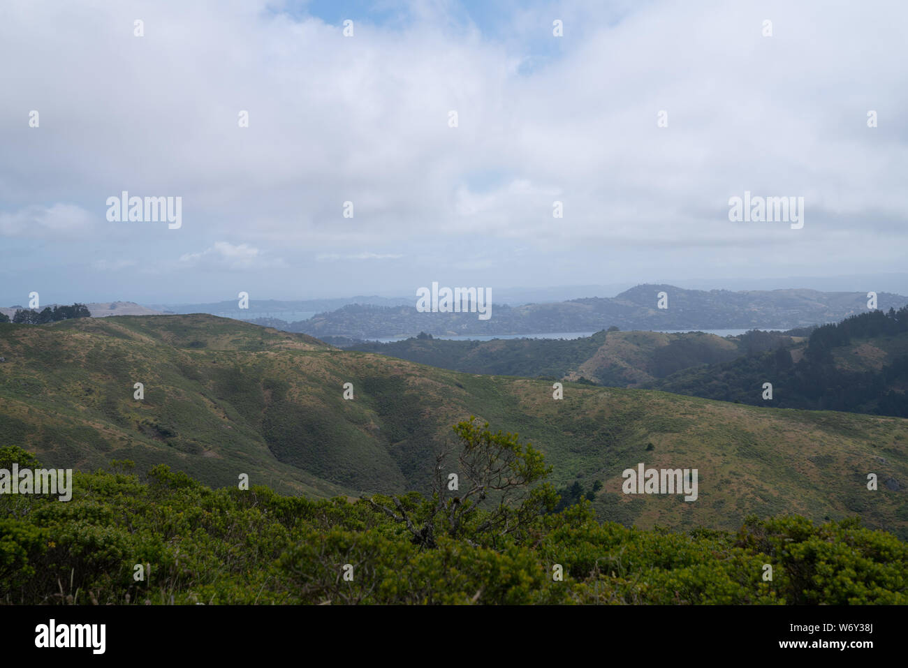Green hills with body of water and cloudy overcast sky Stock Photo