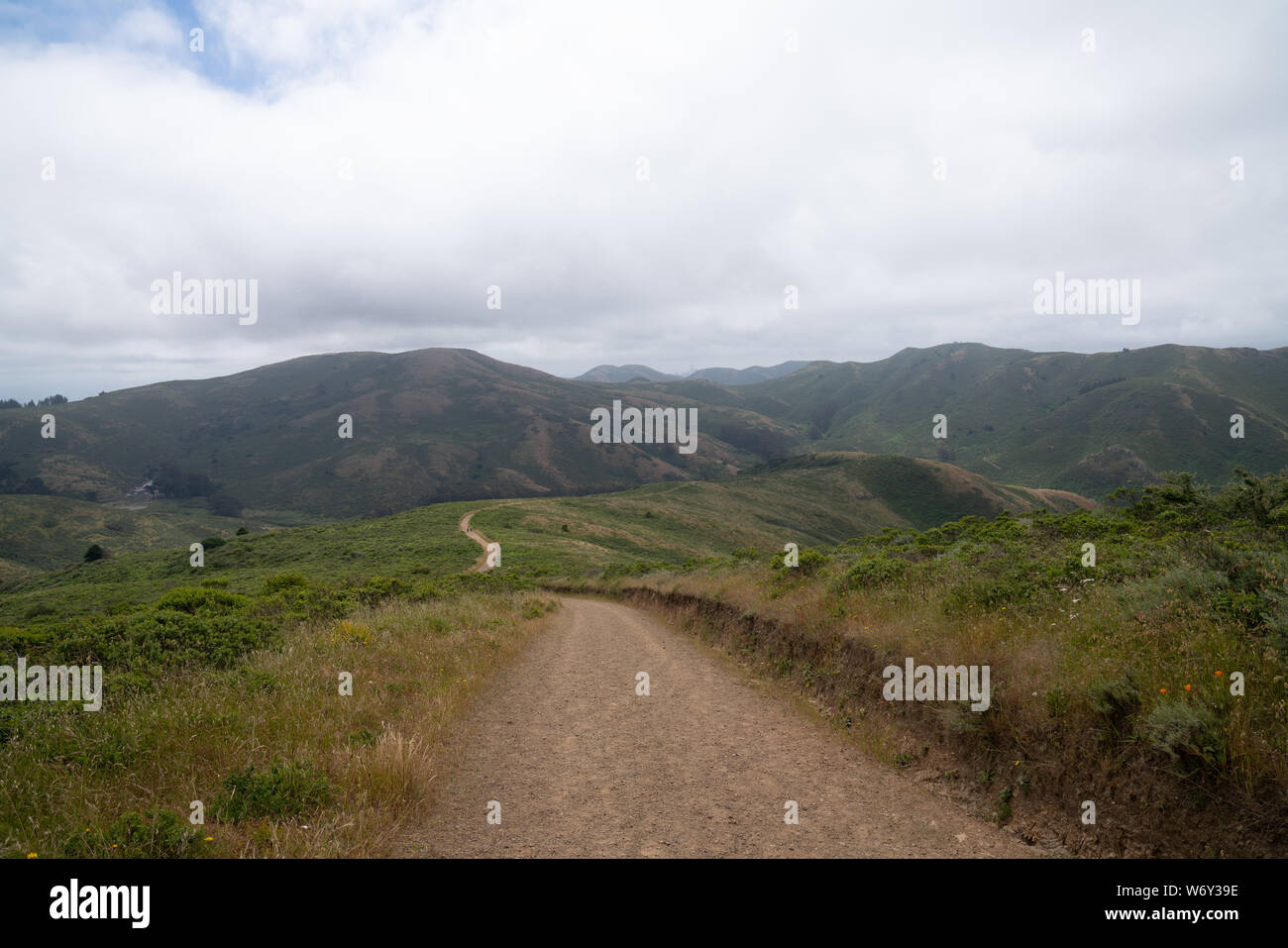 Dirt hiking path on a trail hike with large hills with a brooding overcast sky Stock Photo