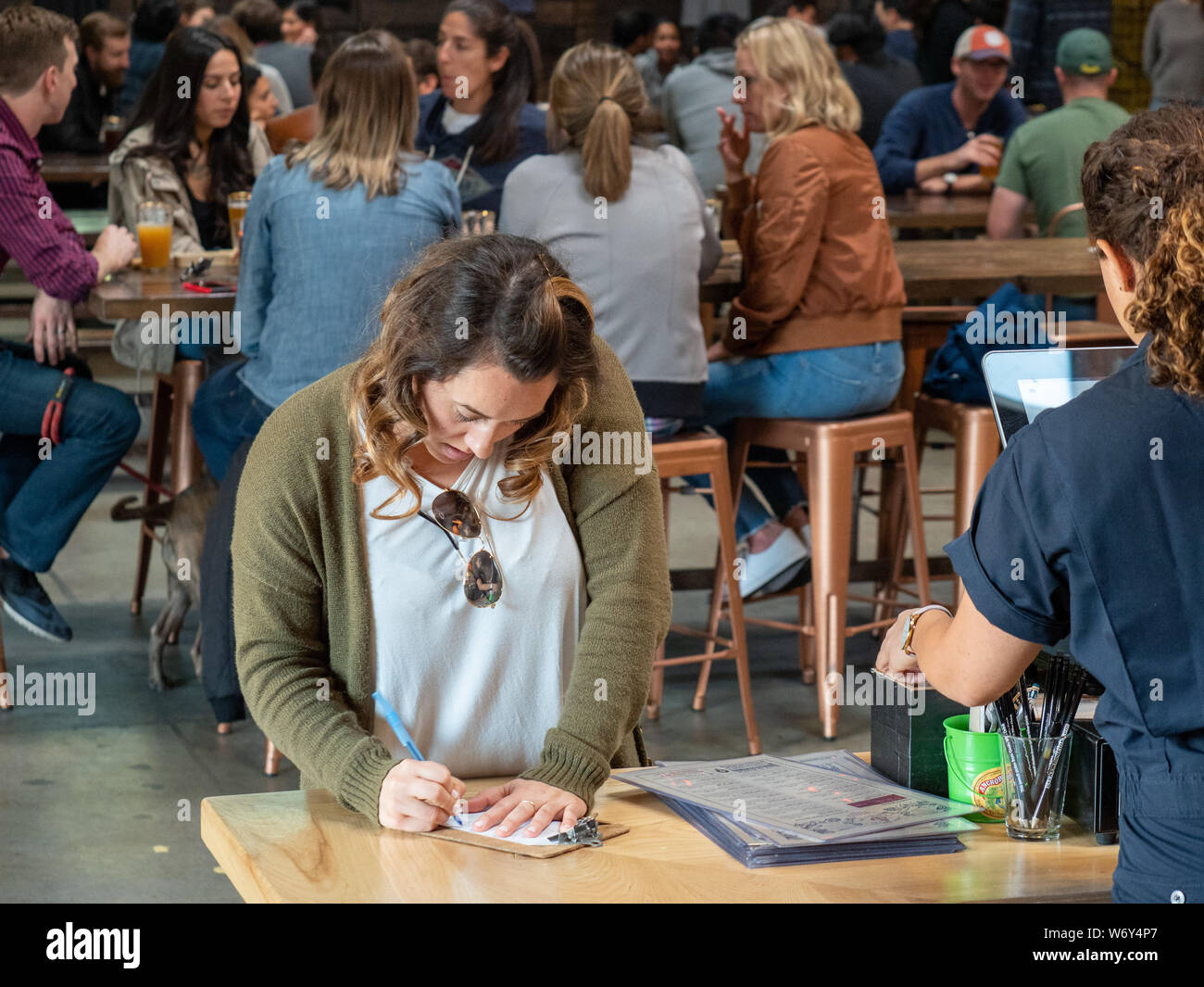 Woman signing receipt at register at popular and crowded bar Stock Photo