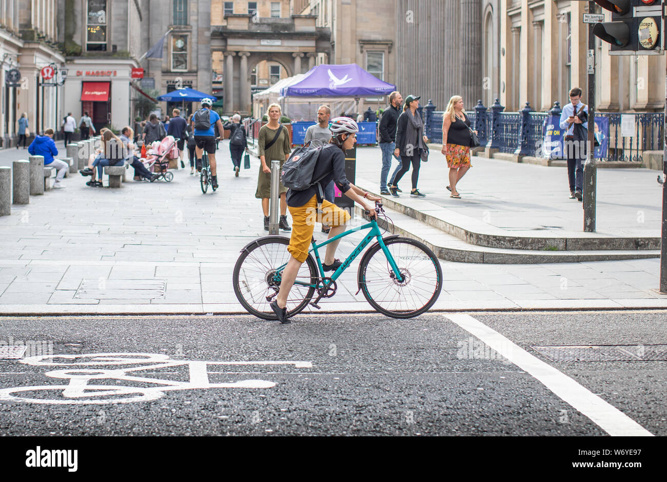 A woman cyclist commuter in central Glasgow cycles past a pedestrianized zone in the Merchants Quarter Stock Photo
