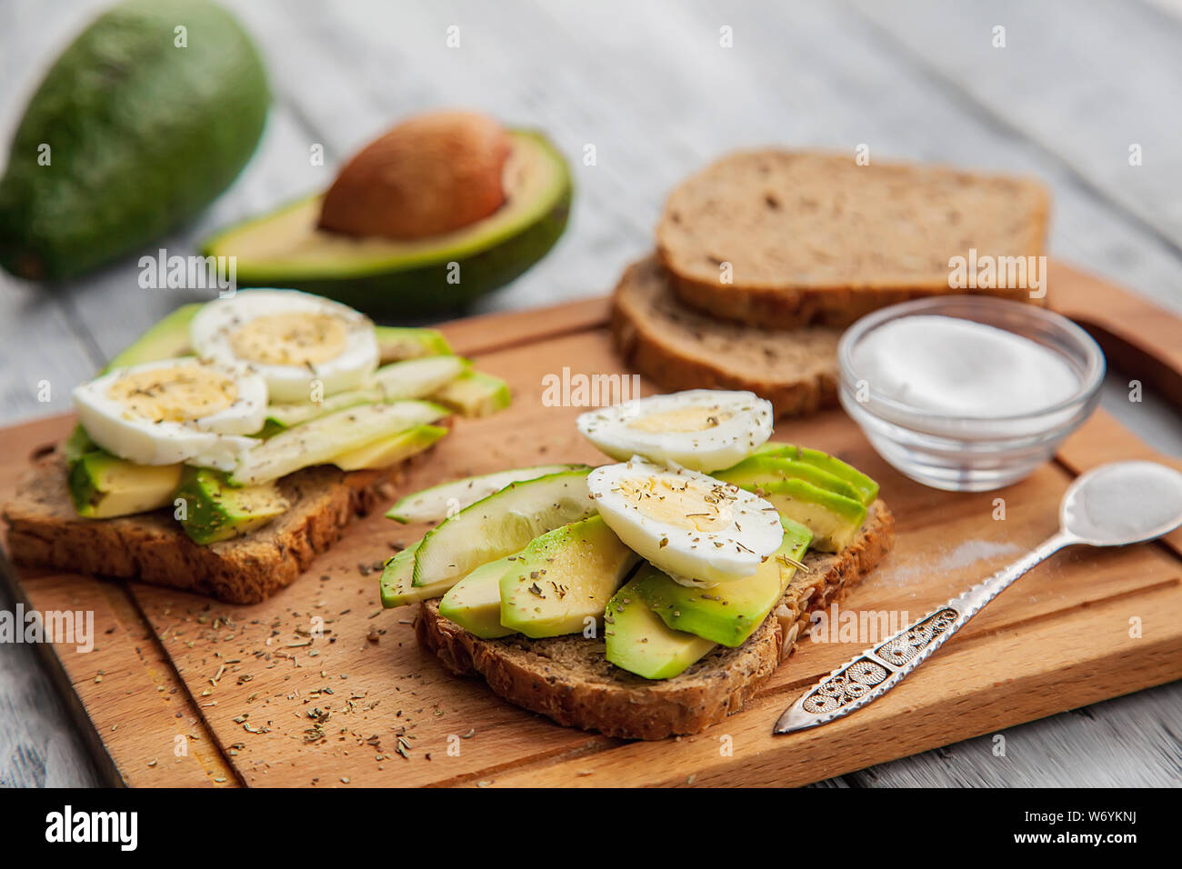 two sliced tasty avocado sandwiches with egg and spices on a wooden Board. Concept of Keto diet Stock Photo