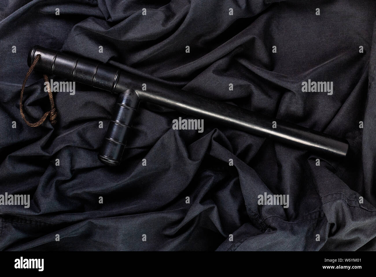 black rubber police baton on black shirt wrinkled cloth low-key flat ...
