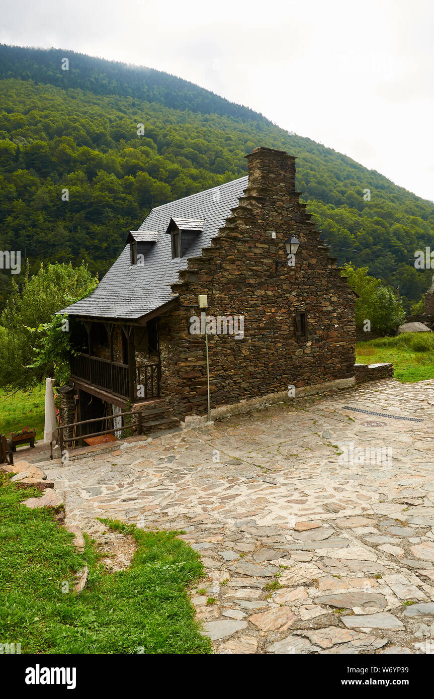 Old stone wall and slate roof renovated house and beech forest in the back (Sant Joan de Toran, Aran valley, Lleida, Pyrenees, Cataluña, Spain) Stock Photo