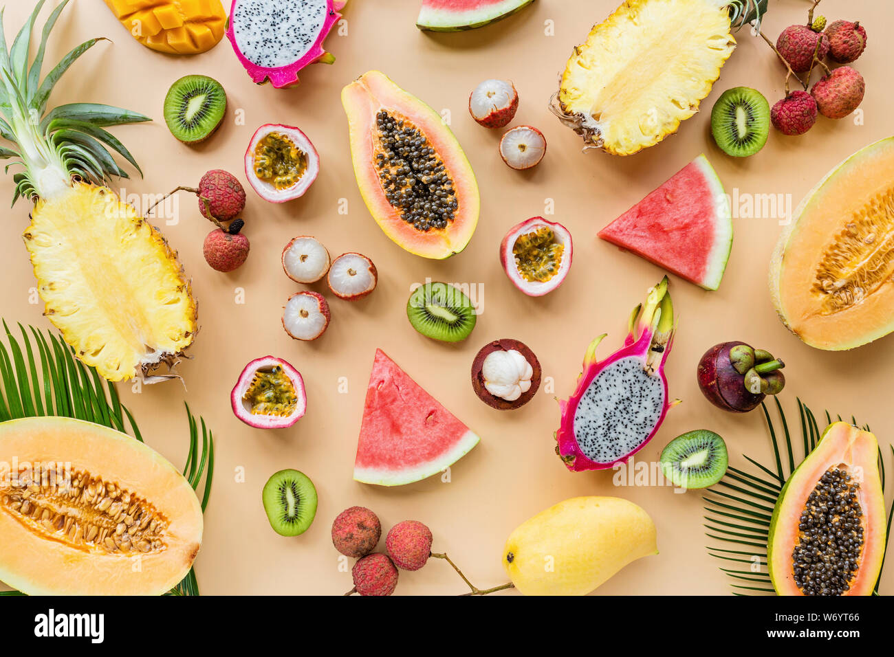 Fresh exotic fruits and tropical palm leaves on pastel orange background papaya, mango