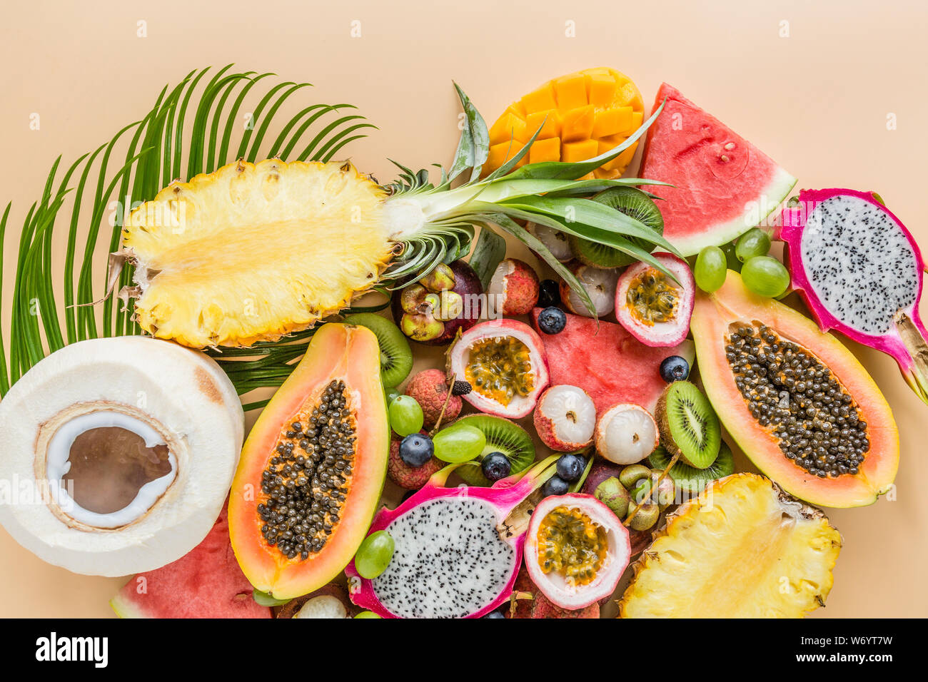 Fresh exotic fruits and tropical palm leaves on pastel orange
