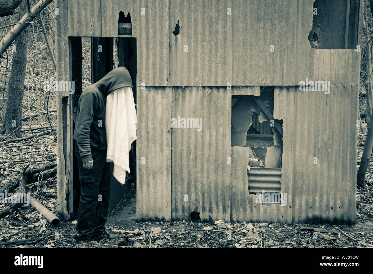 A strange hooded figure with a white sheet covering his face. Standing next to an abandoned forest hut in winter. Stock Photo