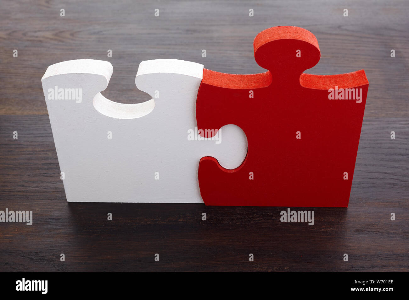 Two white and red details of puzzle on dark wooden background. Stock Photo