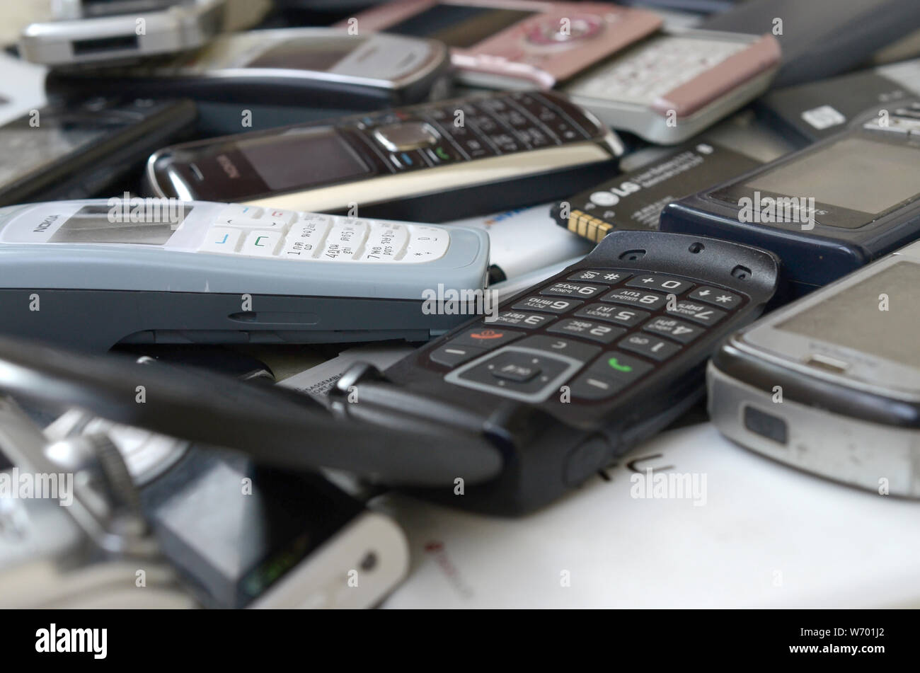 KHARKIV, UKRAINE - JULY 30, 2019: Bunch of old used outdated mobile phones and batteries. Recycling electronics of many brands lies in big pile close Stock Photo