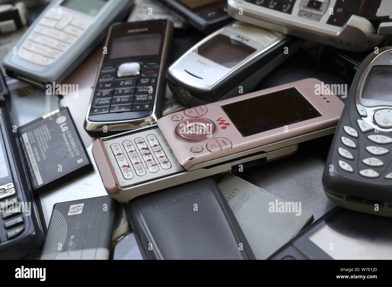 KHARKIV, UKRAINE - JULY 30, 2019: Bunch of old used outdated mobile phones and batteries. Recycling electronics of many brands lies in big pile close Stock Photo