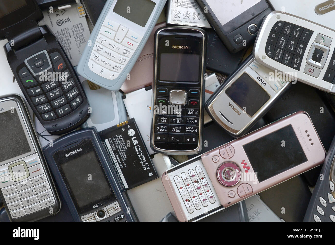 KHARKIV, UKRAINE - JULY 30, 2019: Bunch of old used outdated mobile phones and batteries. Recycling electronics of many brands lies in big pile close Stock Photo