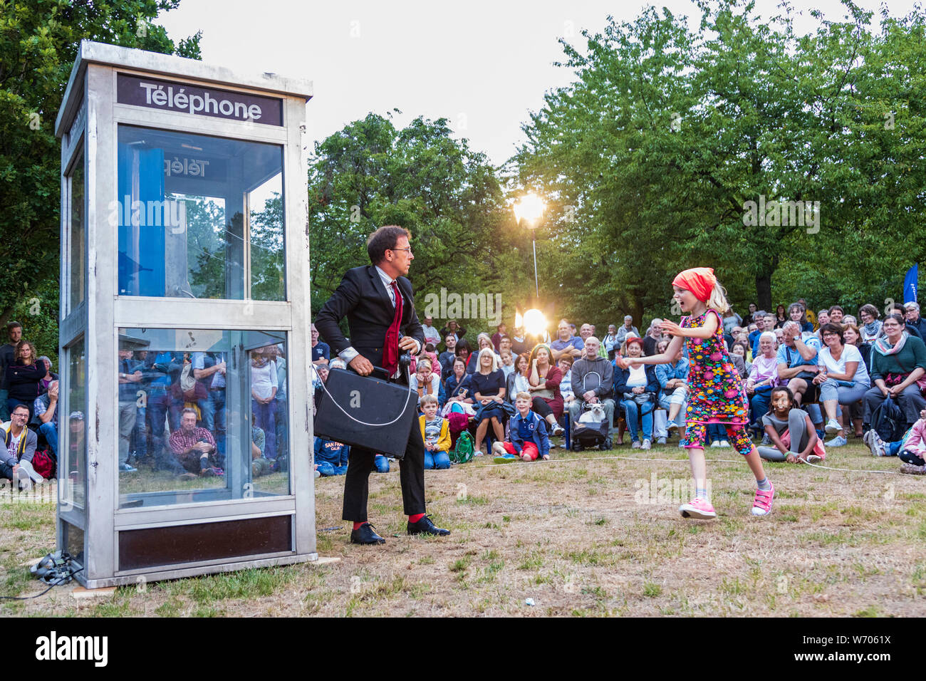 Mülheim an der Ruhr, Germany. 3 August 2019. Frenchman Ivan Chary of the Compagnie du Petit Monsieur tries to get into a closed telephone box and receives help from a young member of the audience. The 11th Broicher Schlossnacht takes places with performances ranging from dance to arts and theatre at MüGa-Park. Photo: Vibrant Pictures/Alamy Live News Stock Photo