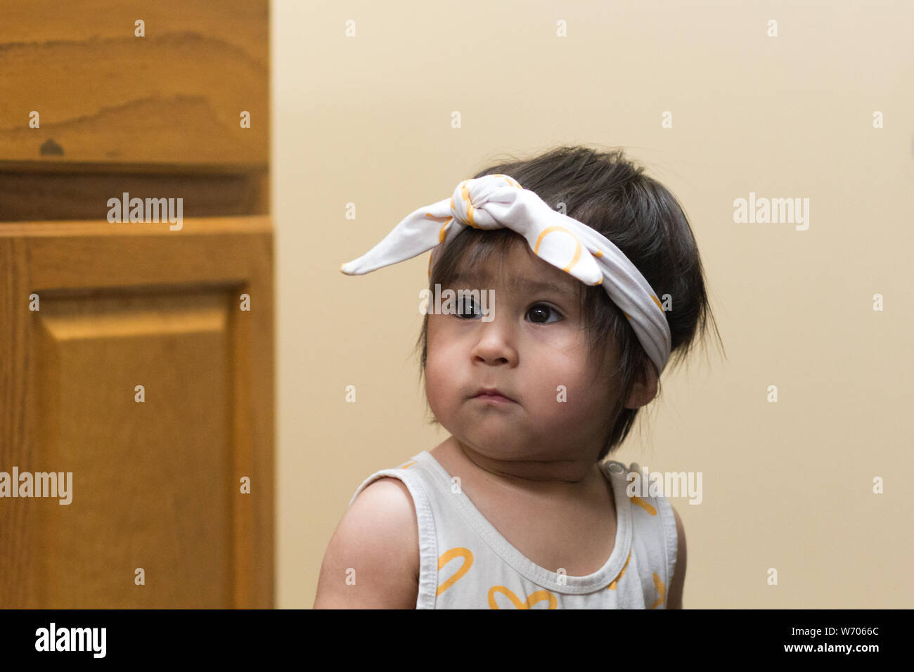 A female Hispanic baby or toddler, wearing a scarf on her head, looks to the side Stock Photo
