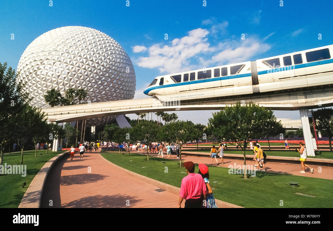 A Walt Disney World monorail train glides above visitors heading to a huge geodesic sphere called Spaceship Earth that is the symbol of Epcot, one of four theme parks within the world-famous Disney amusement complex near Orlando in Florida, USA. Epcot is an acronym for Experimental Prototype Community of Tomorrow and was originally planned to be a utopian city. However, it has evolved  into two themed areas: Future World, showcasing science and technology, and World Showcase, featuring the lifestyles of 11 different countries. Since opening in 1971, Disney World has become an American icon. Stock Photo
