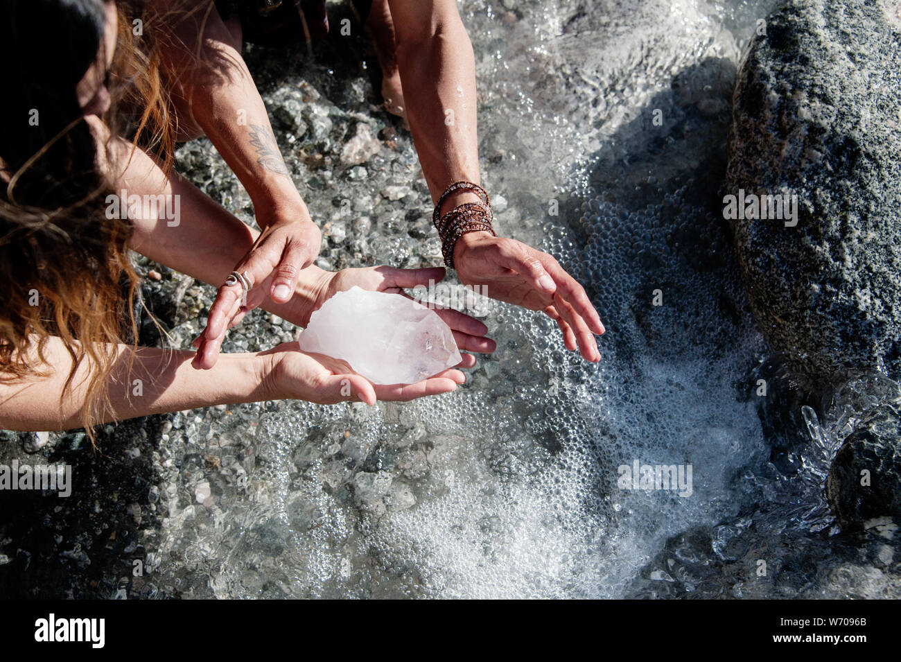 The hands of two women cleanising a big quartz crystal in a wild river. Stock Photo