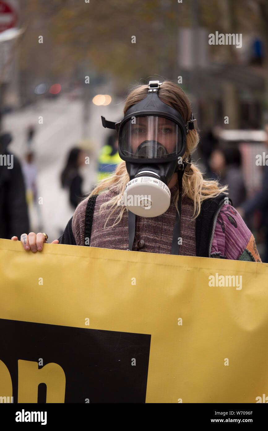 Woman wearing a black gas mask holding a bright yellow Climate Emergency banner disruption traffic in downtown Melbourne, Australia. Stock Photo