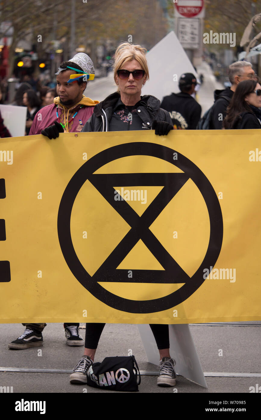 Young blonde woman in black sunglasses and black leather jacket defiantly holding holding a large yellow Climate Emergency banner. Stock Photo