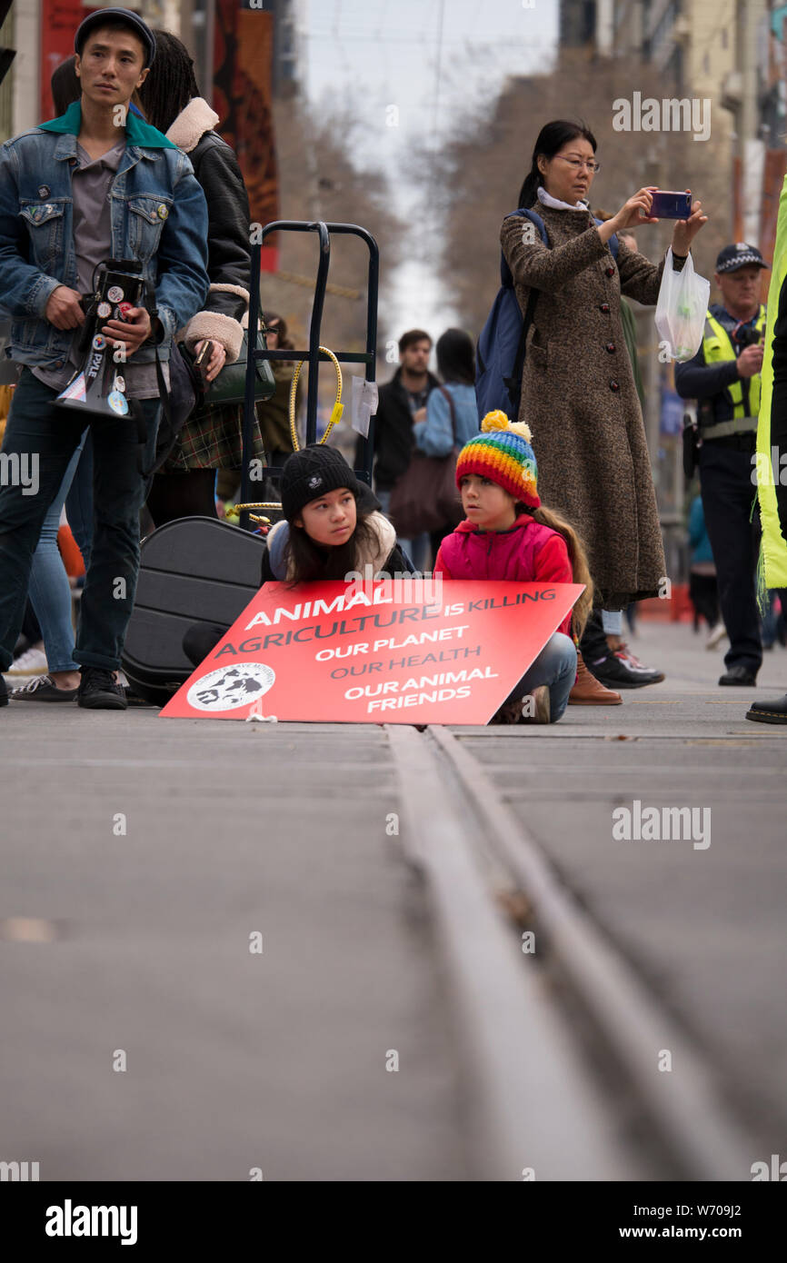 Two young children sitting on tram tracks with red Climate Emergency sign at demonstration in downtown Melbourne, Australia climate protest. Stock Photo