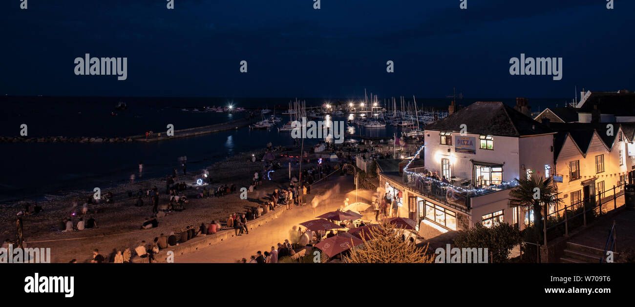 Lyme Regis, Dorset, UK. August 2019. UK Weather: Crowds gather on a warm summer evening to watch the annual August firework display at the Cobb harbour Lyme Regis.  The charity event takes place every year as part of the Regatta, Carnival and Lifeboat week and is attended by locals and visitors to the town with many returning year on year.  Credit: Celia McMahon/Alamy Live News. Stock Photo