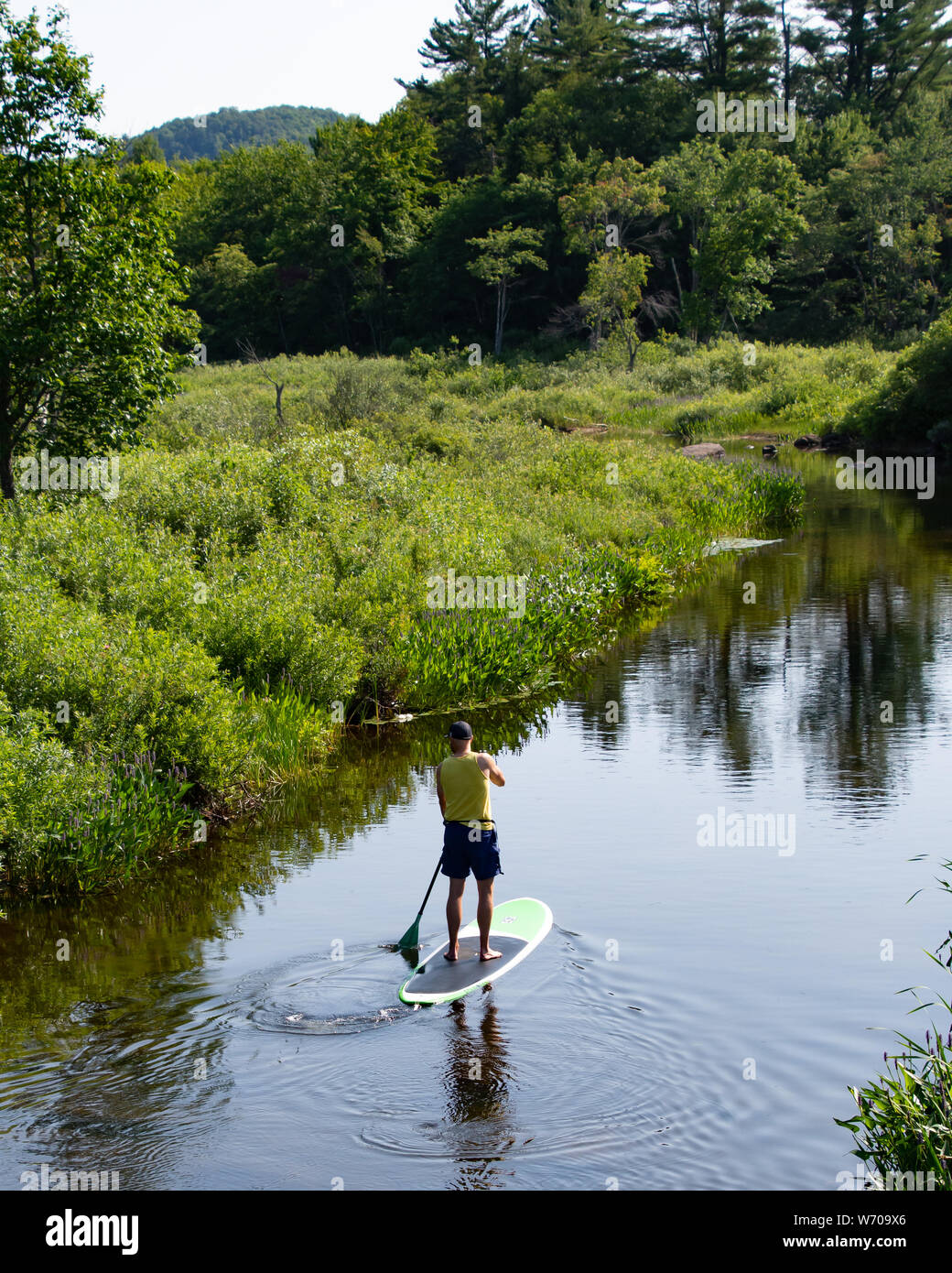 A man paddling a paddle board on the Sacandaga River at the outlet from Lake Pleasant in the Adirondack Mountains, NY USA Stock Photo