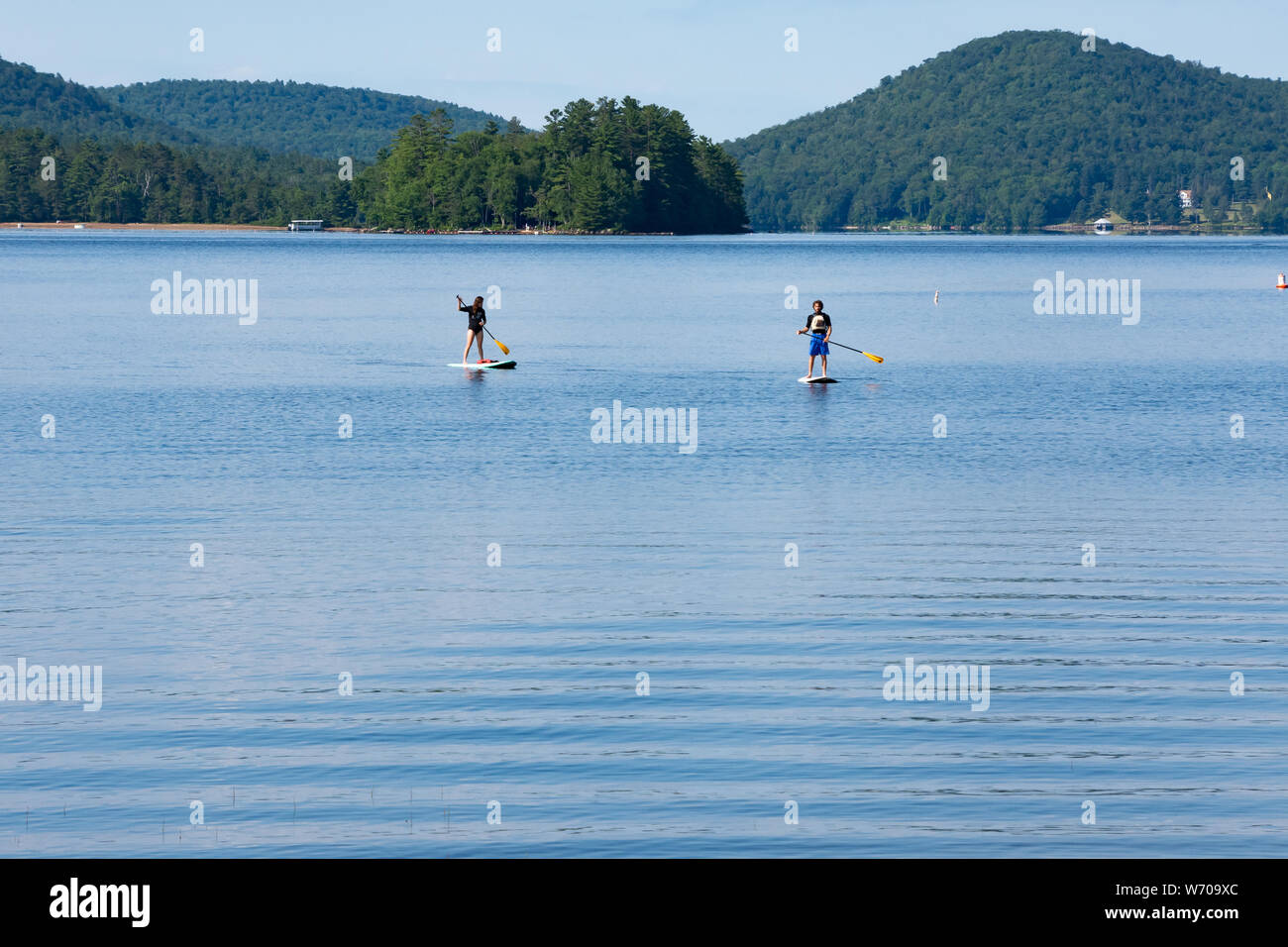 A man and a woman paddling paddle boards on Lake Pleasant in the Adirondack Mountains, NY USA with the island Tapawingo in the background. Stock Photo