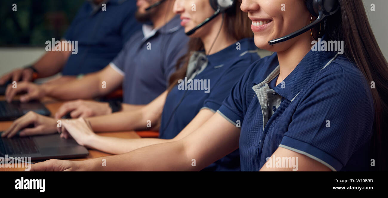 Smiling people in customer service talk with headphones and type on laptop Stock Photo