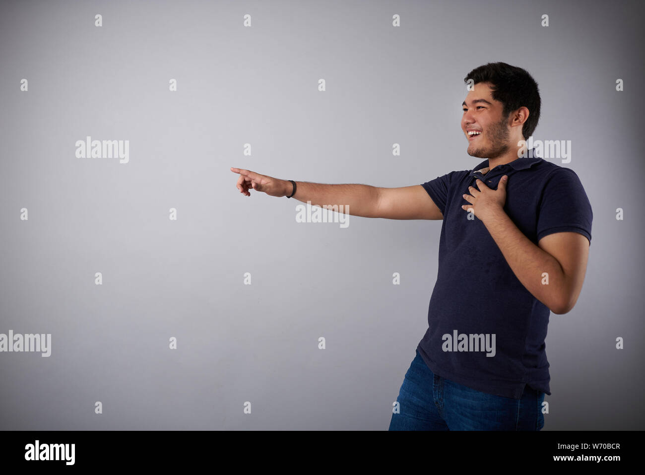 Laughing young man and point finger on side in studio background Stock Photo