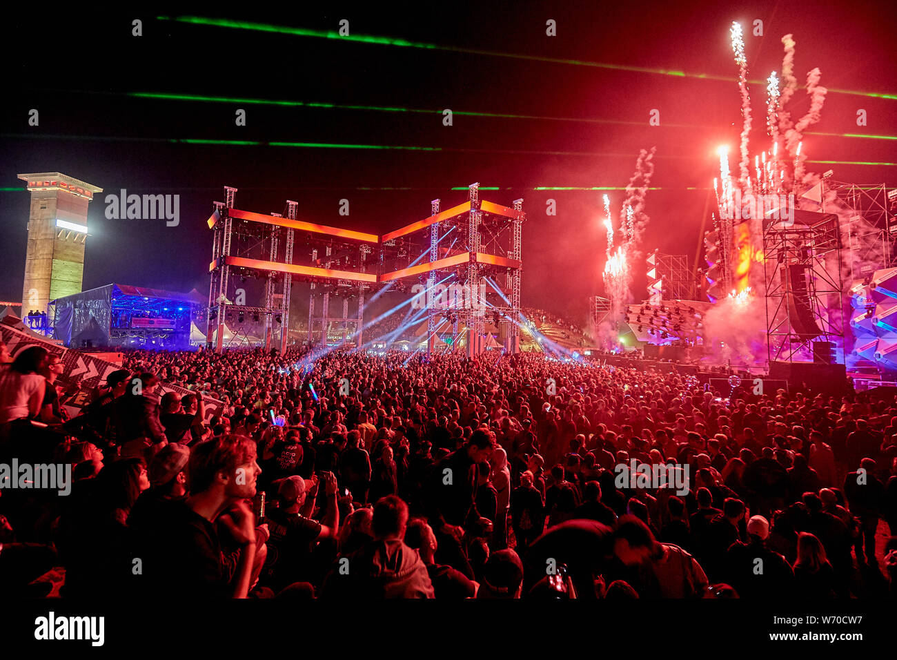 Kastellaun, Germany. 03rd Aug, 2019. The light of the stage lasers can be seen at the 25th anniversary of techno festival "Nature One" in the Hunsrück behind the watchtower of the