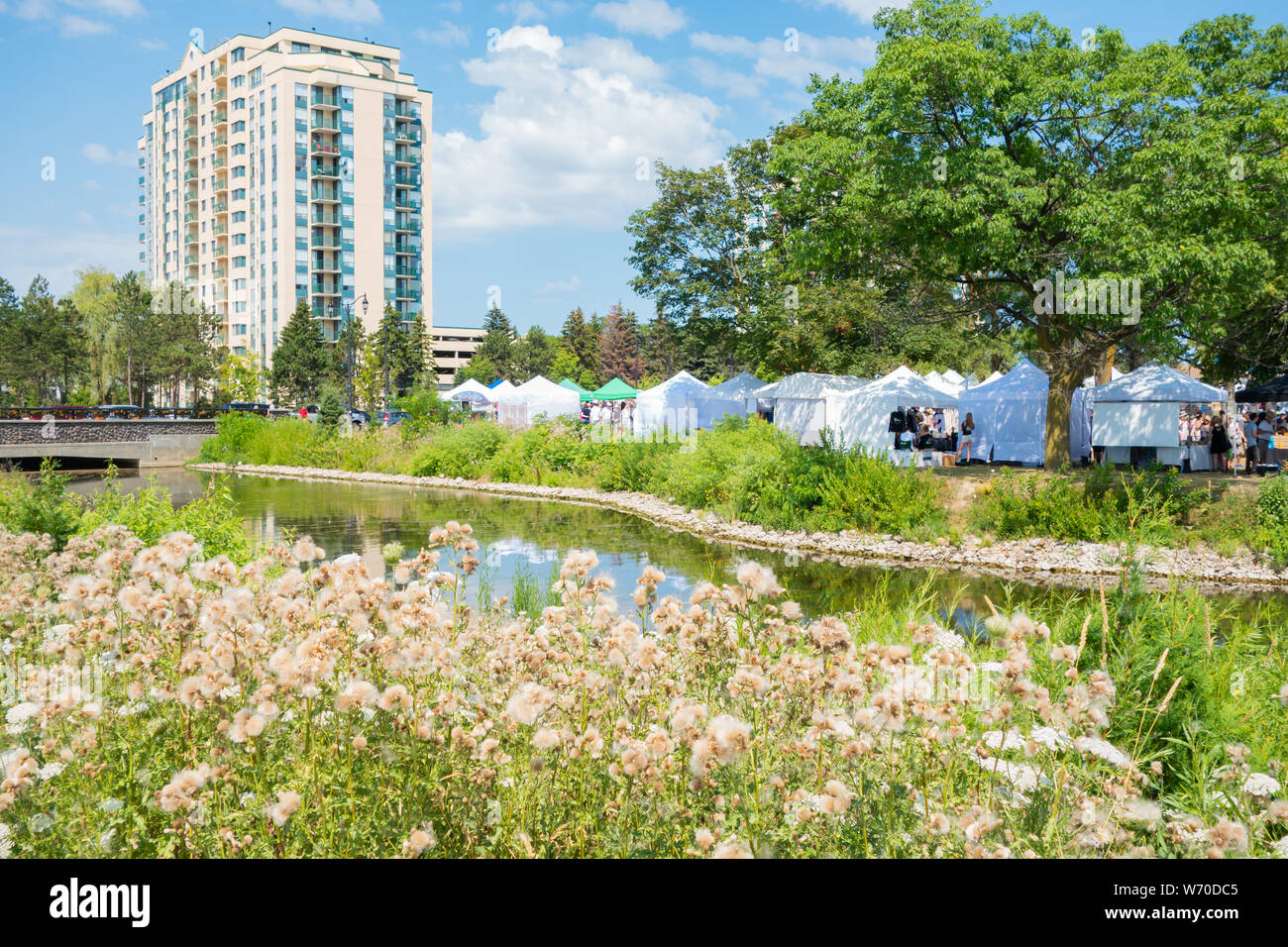 Pretty creek flows into Kempenfelt Bay with the vendor booths of Kempenfest in the background. Stock Photo