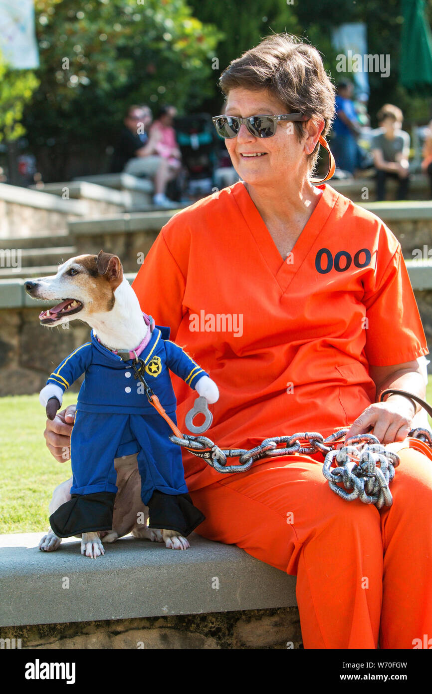 Sandy Springs, GA, USA - September 22, 2018:  A jack russell terrier dressed as a prison guard is chained to its human owner, dressed in an orange pri Stock Photo