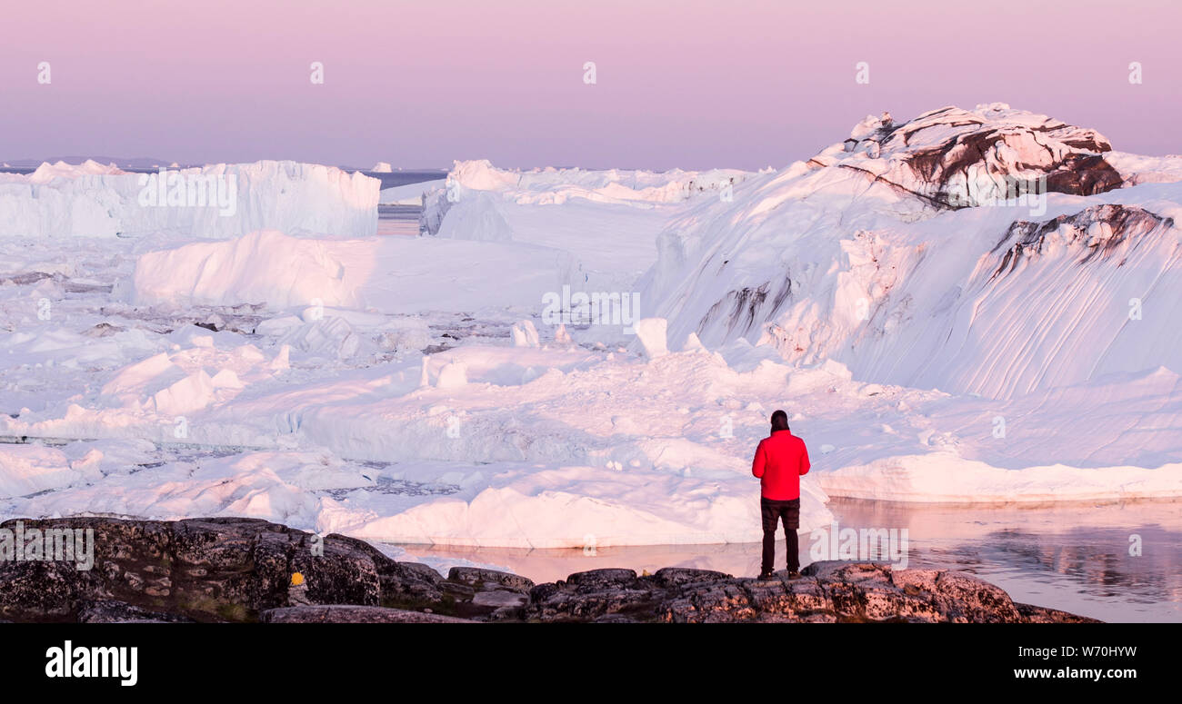 Travel in arctic landscape nature with icebergs - Greenland tourist man explorer - tourist person looking at amazing view of Greenland icefjord - aerial drone image. by ice iceberg, Ilulissat