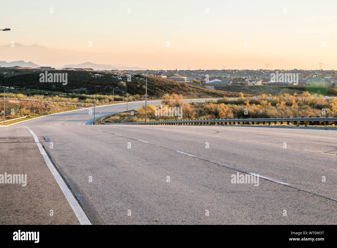 paved rural street and roadway with curve and guardrail in golden light ...