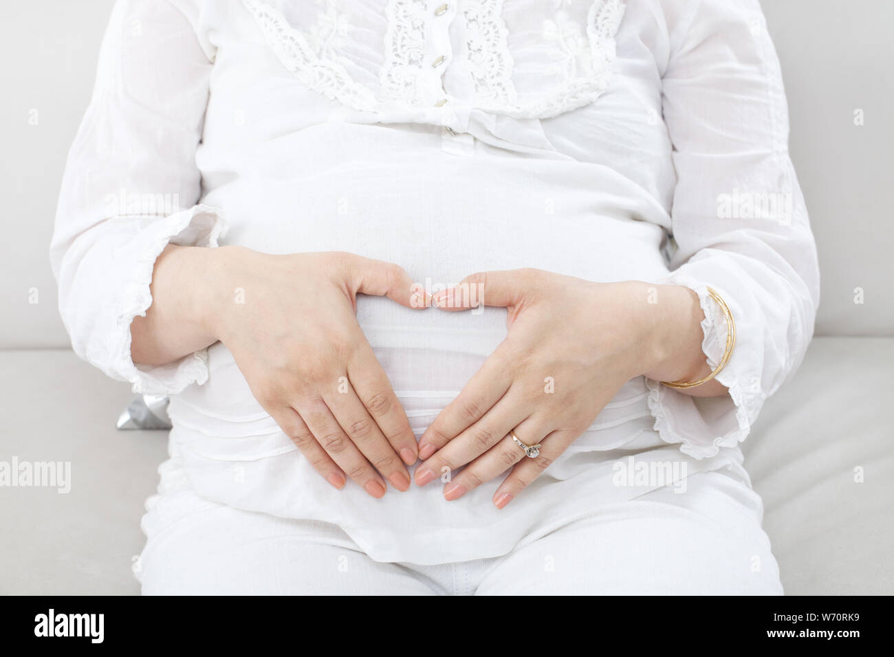 Pregnant woman holding her tummy with her fingers forming a heart shape Stock Photo