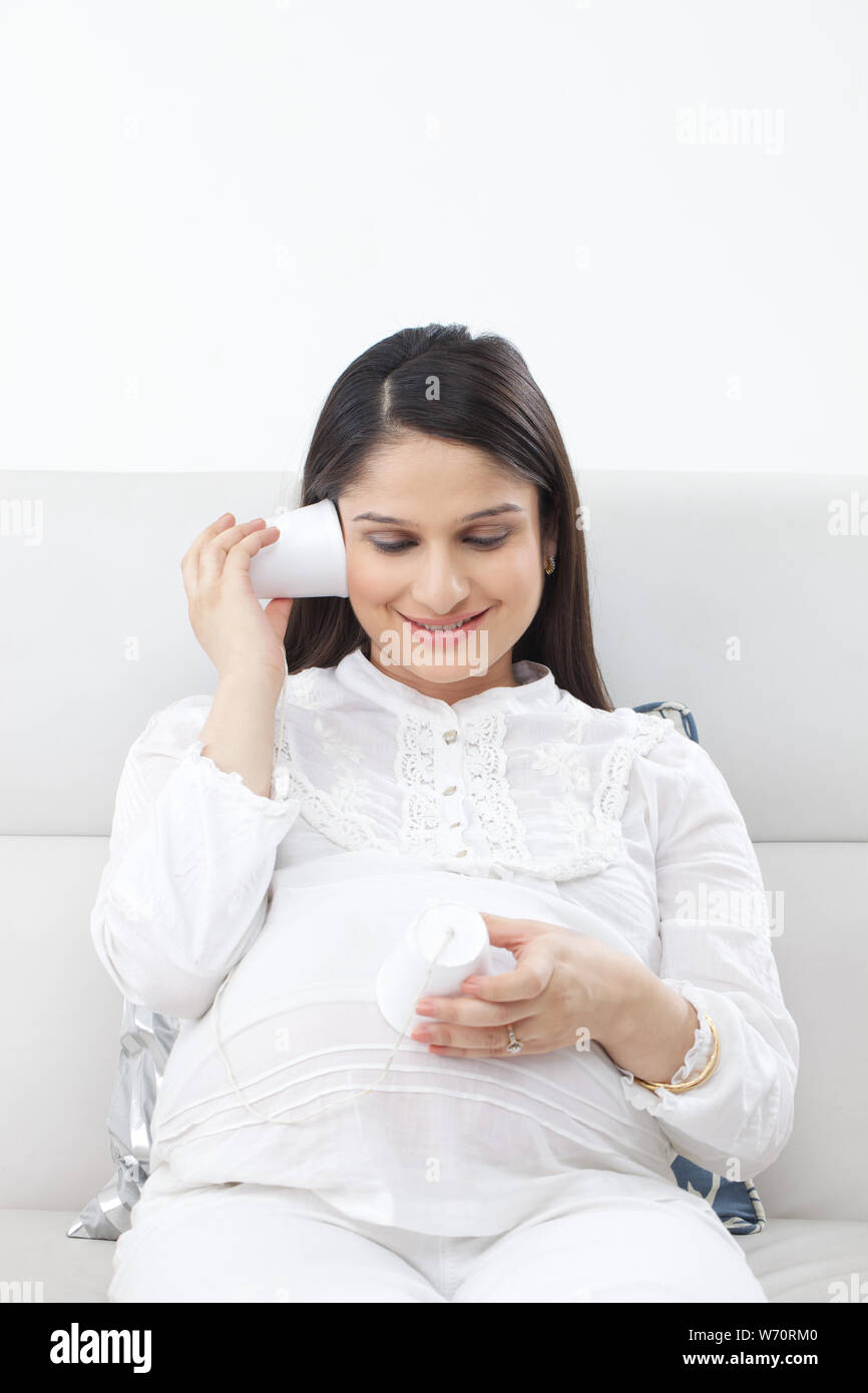 Pregnant woman holding tin can phone to ear Stock Photo