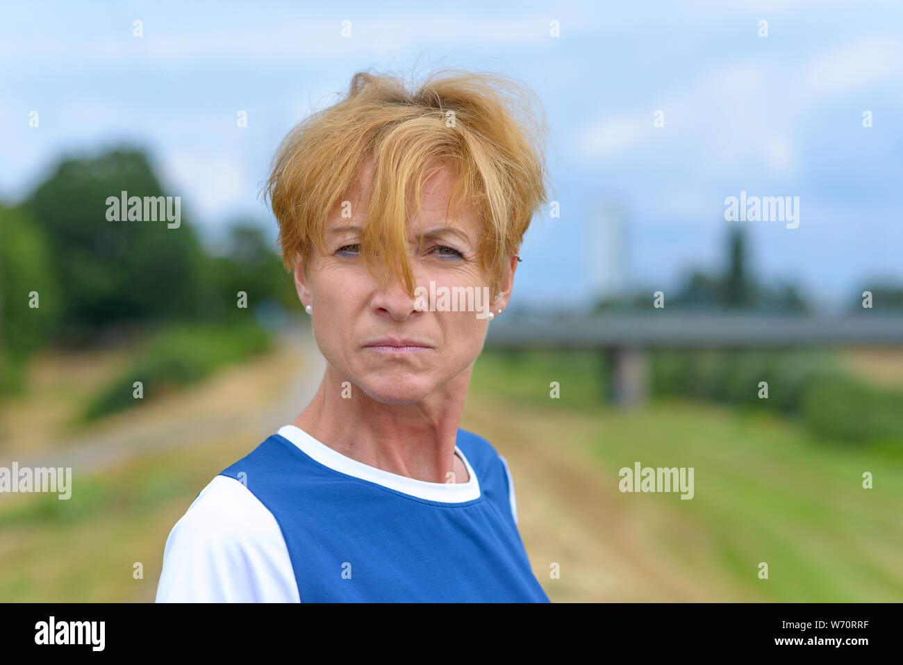 Upset angry woman glaring at the camera with an intense expression with her red blond hair falling over her nose outdoors in countryside Stock Photo