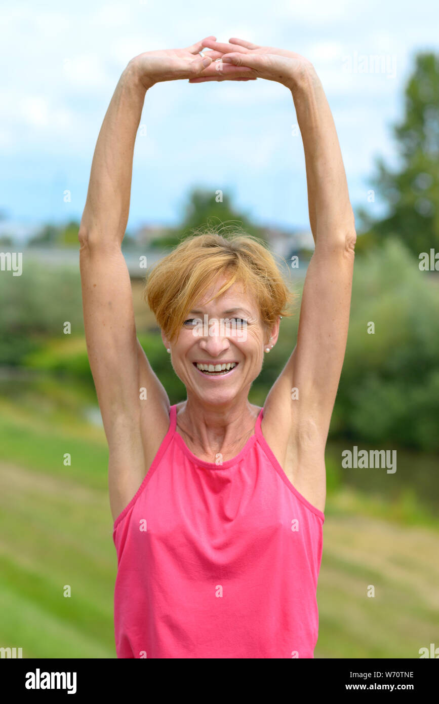 Happy vivacious woman stretching her arms above her head while laughing at the camera as she rejoices outdoors in summer sunshine Stock Photo