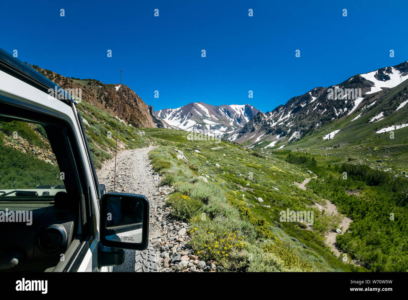 Jeep on dirt road in Sierras with mountain peaks and green valley Stock