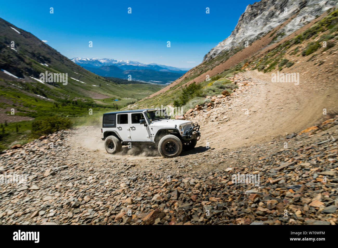 Jeep on dirt road in Sierras with mountain peaks and green valley Stock
