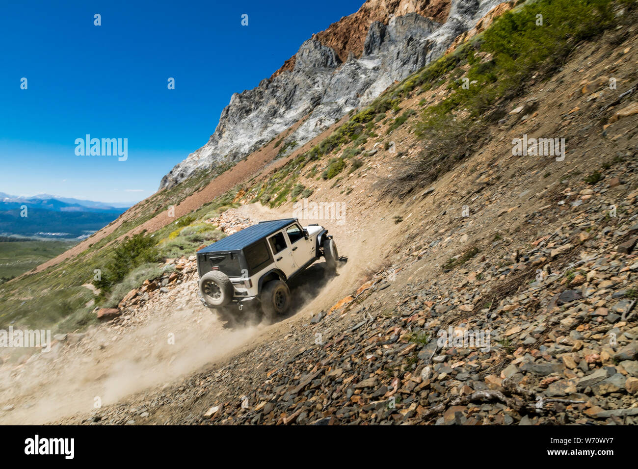 Jeep on dirt road in Sierras with mountain peaks and green valley Stock