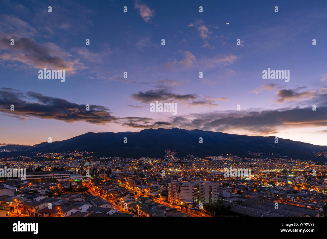 Cityscape of Quito city at sunset with the mighty peaks of the Pichincha volcano and crescant moon, Andes mountains, Ecuador. Stock Photo