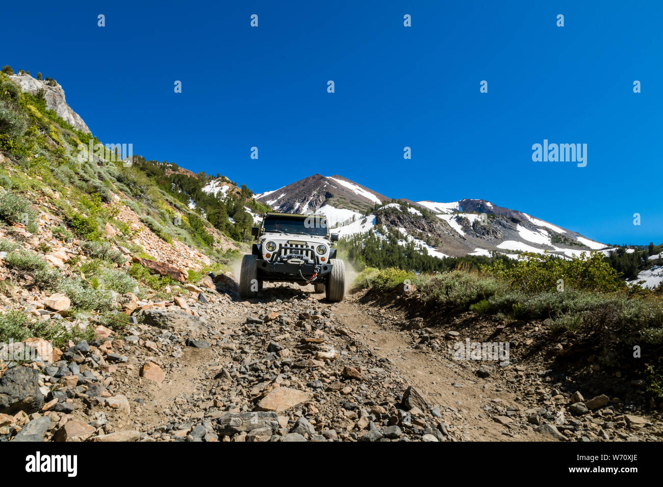 Jeep on dirt road in Sierras with mountain peaks and green valley Stock