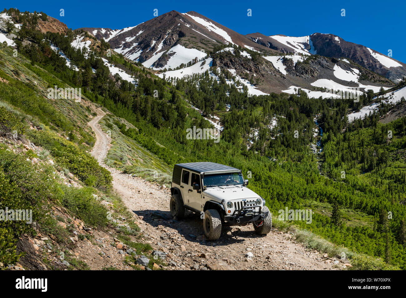 Jeep on dirt road in Sierras with mountain peaks and green valley Stock