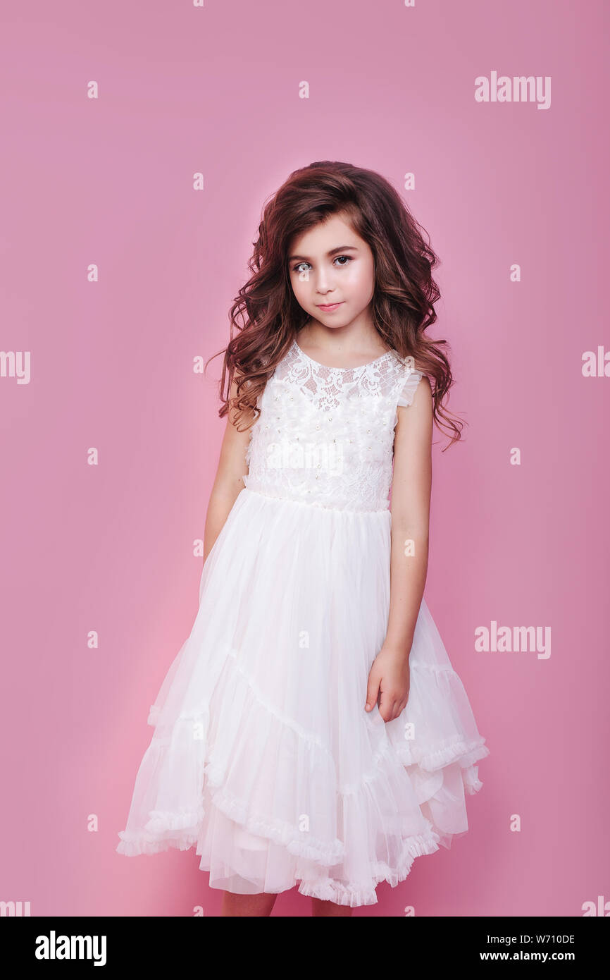 portrait of beautiful little girl in white dress on pink background ...