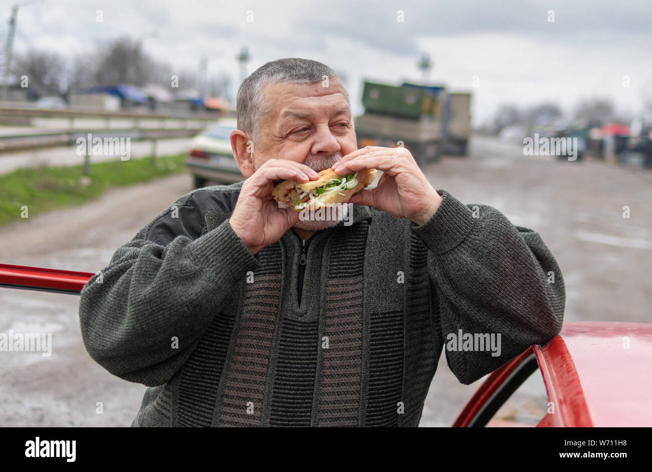 Senior driver gobbling lyulya kebab in lavash near his car standing on a back road Stock Photo