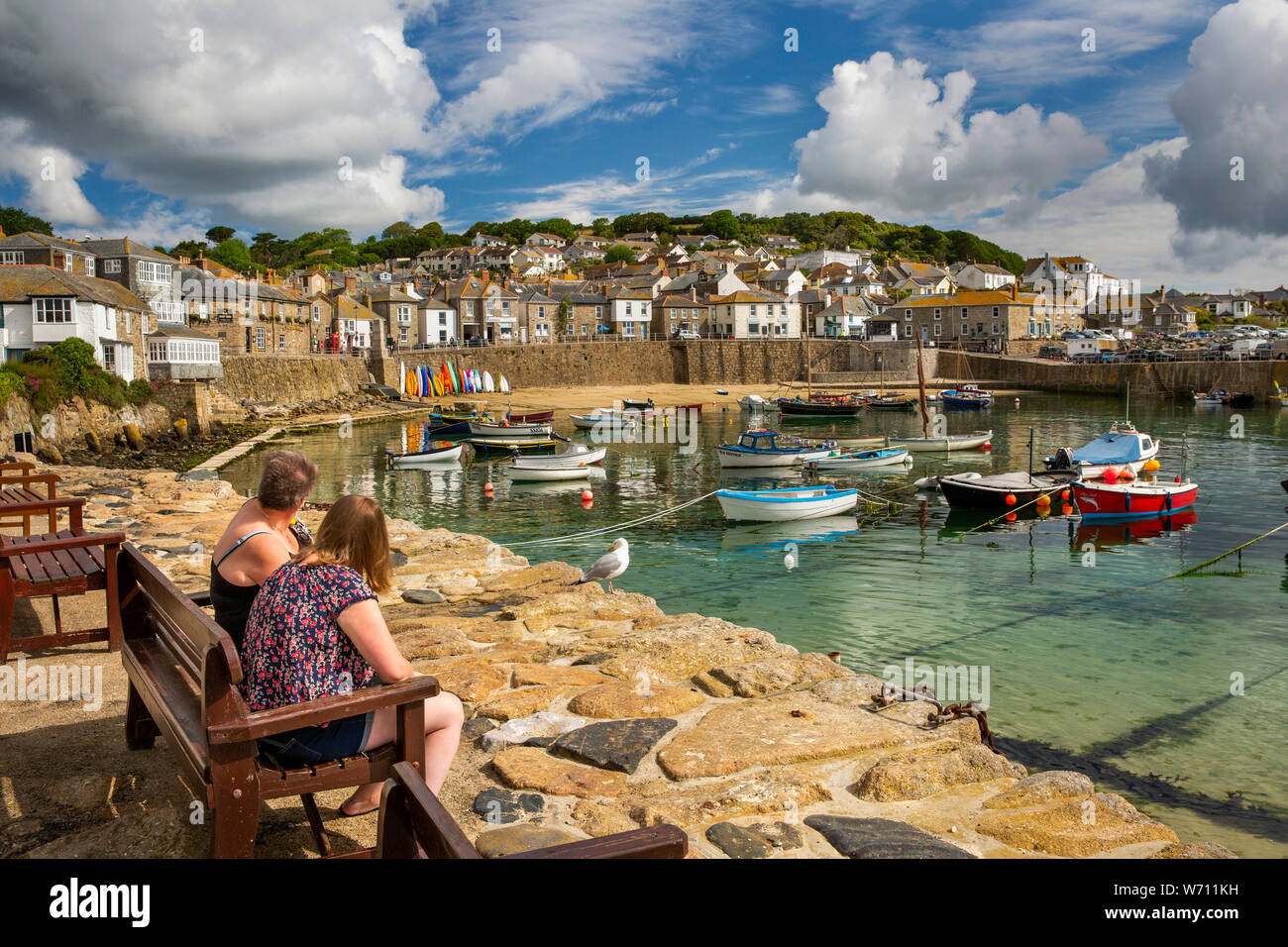 UK, England, Cornwall, Mousehole, The Wharf, couple on quayside bench, admiring boats moored in harbour Stock Photo