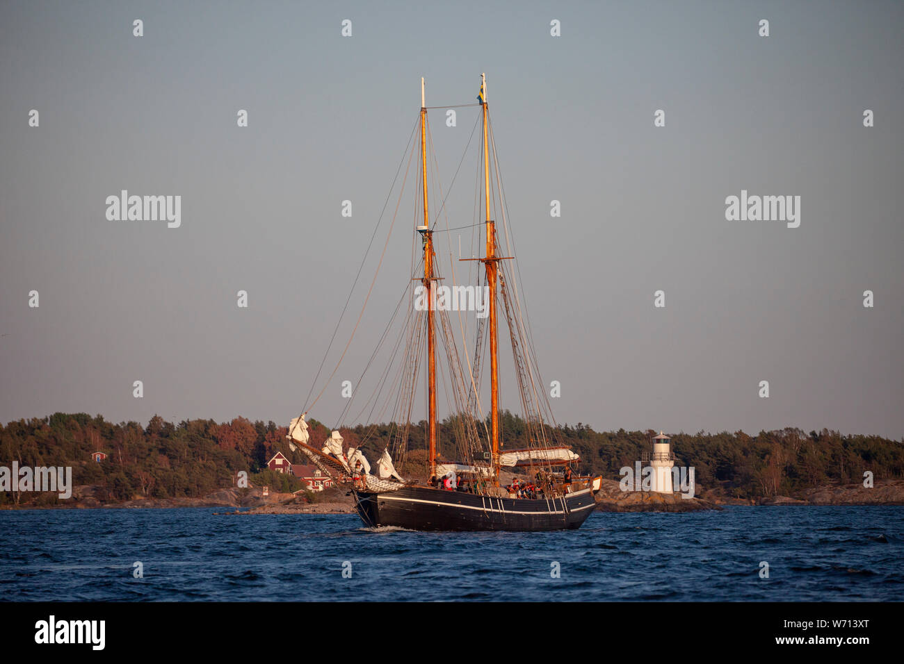 Beautiful wooden ship glides past a lighthouse in the Swedish archipelago Stock Photo
